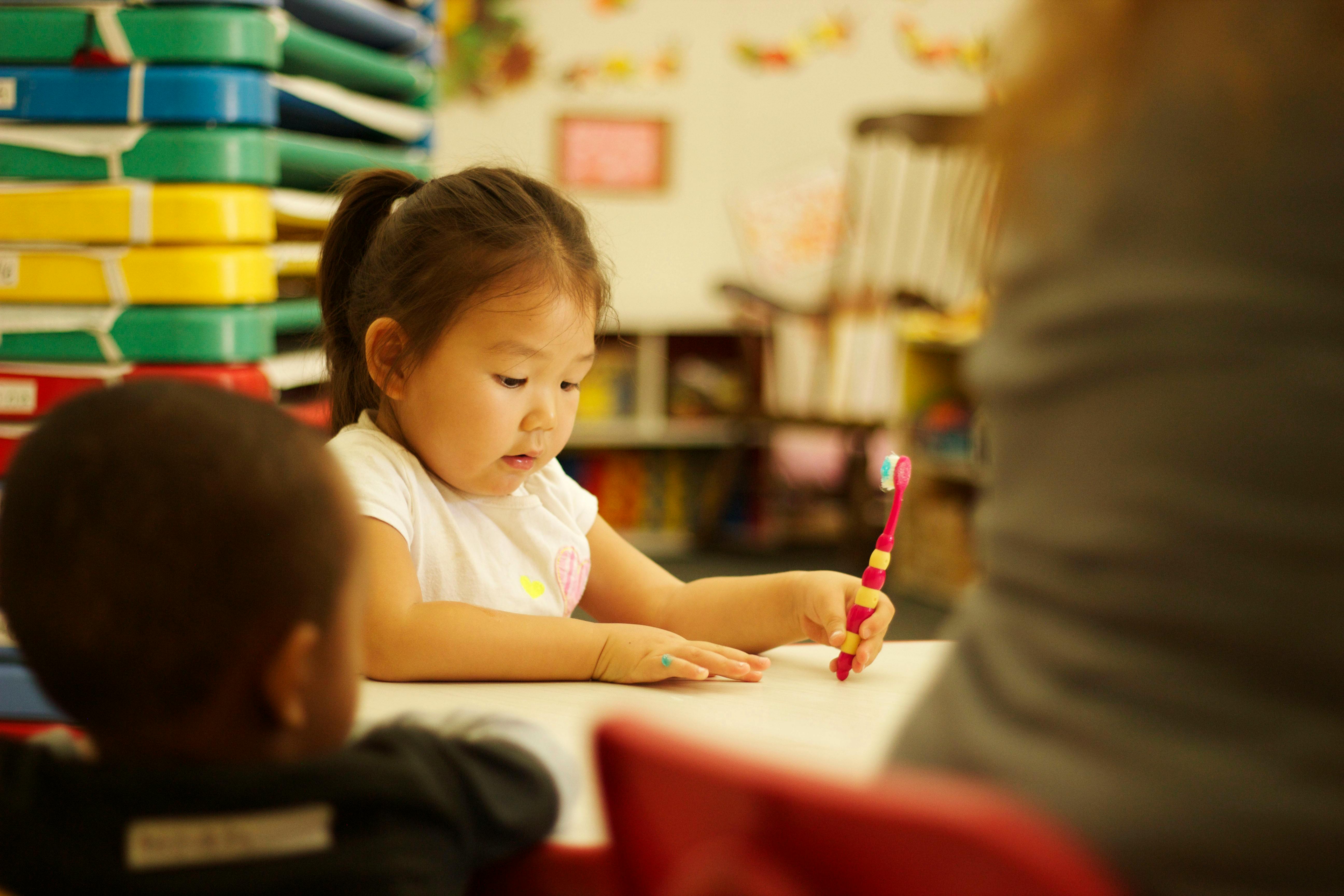 Child holding a red object at a table with another child
