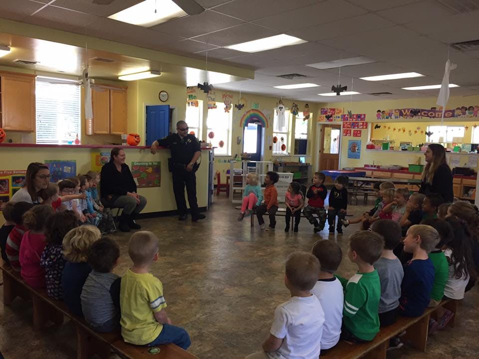 Person in uniform speaking to children and adults in a classroom
