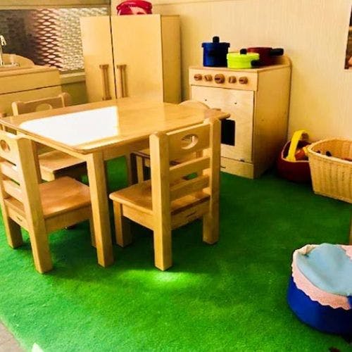 Children's play area with wooden table and chairs, toy kitchen, and baskets