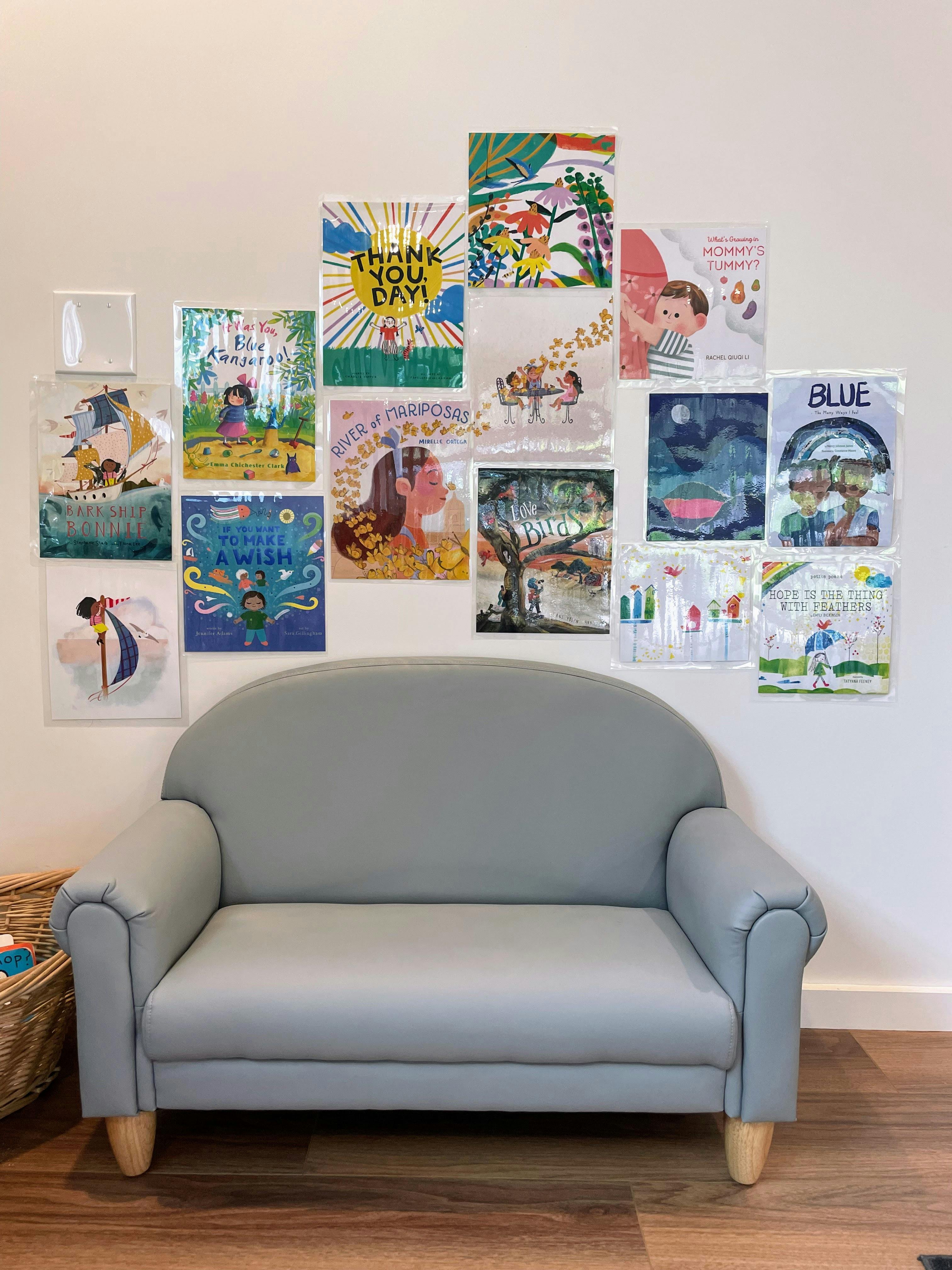 Small gray couch positioned in front of a wall decorated with children book covers