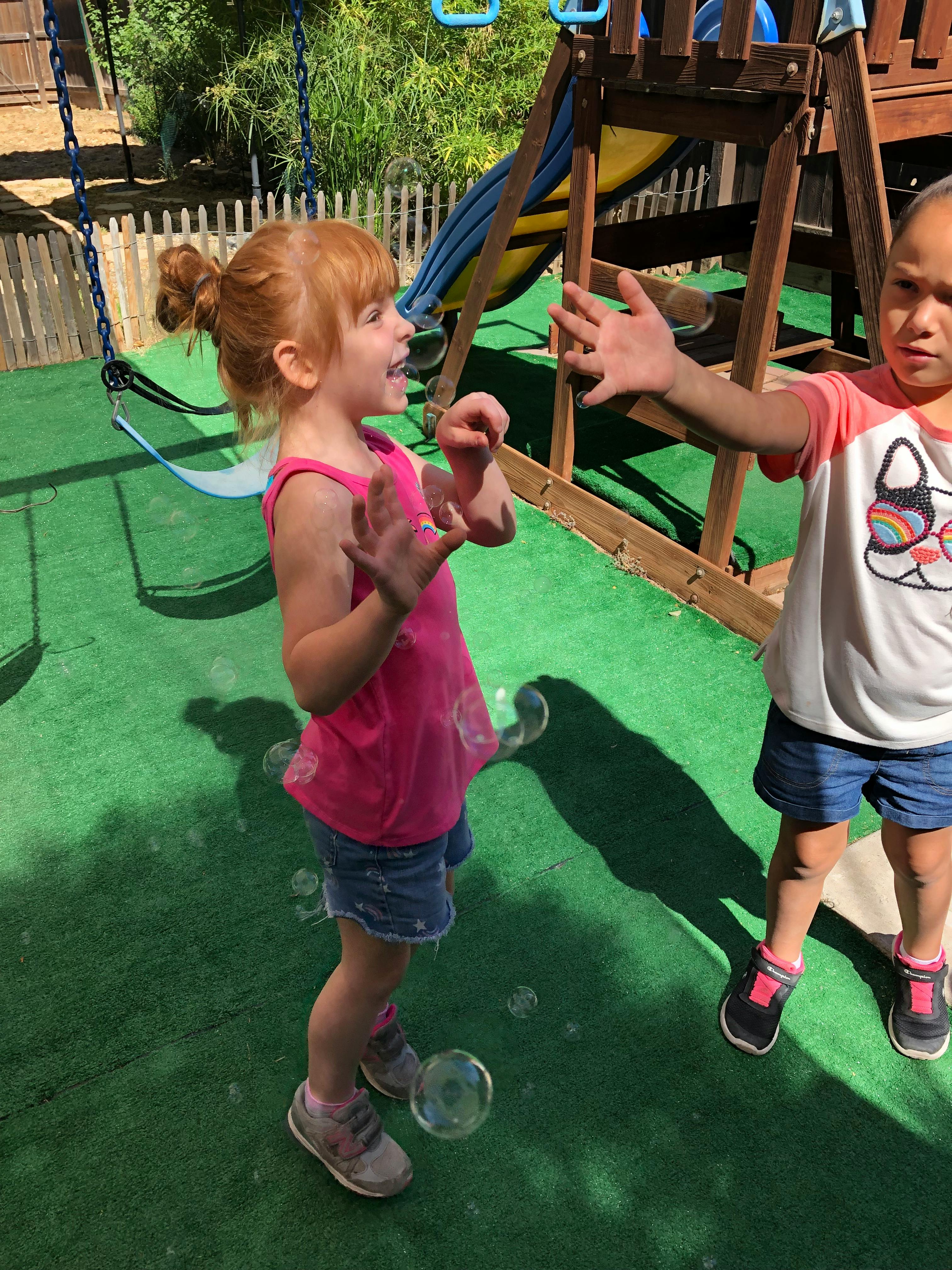 Two children playing with bubbles on a green surface