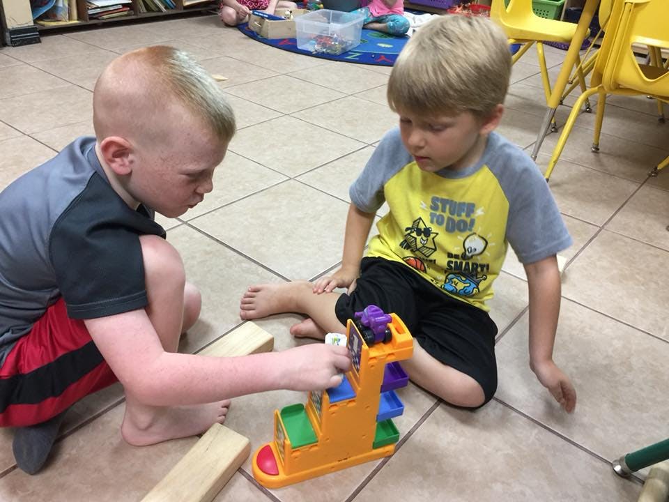 Two children playing with a toy ramp on the floor