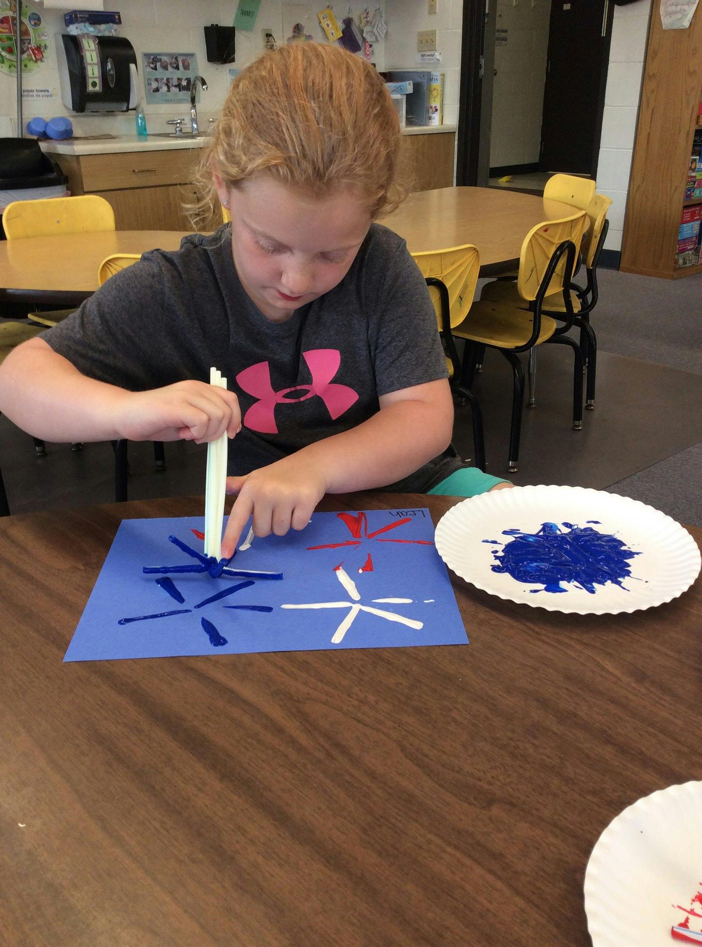 Child making art with paint and paper in a classroom