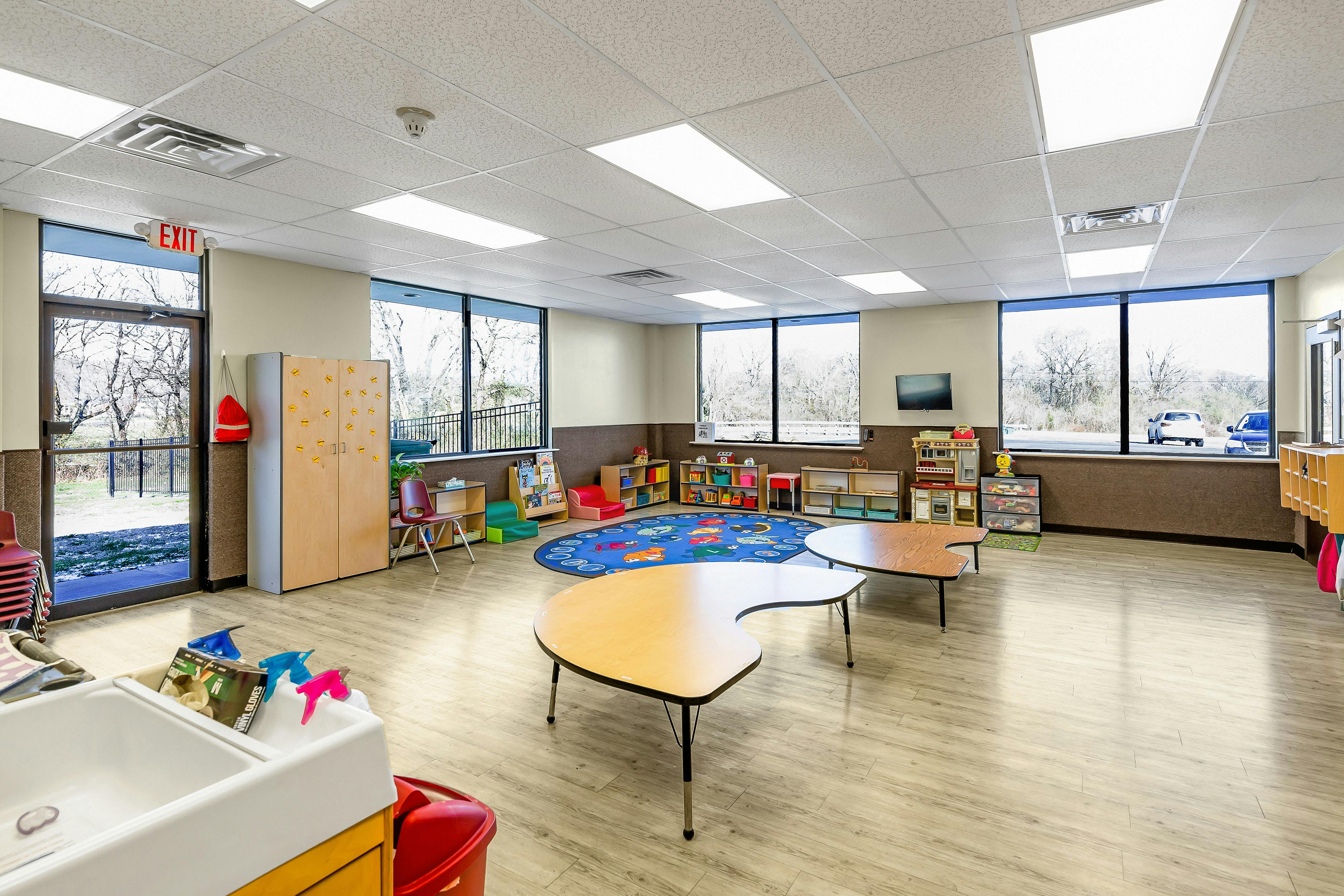 Empty classroom with small tables, a rug, and shelves