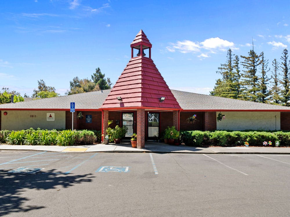 Building with a red pointed roof over the entrance and a parking lot