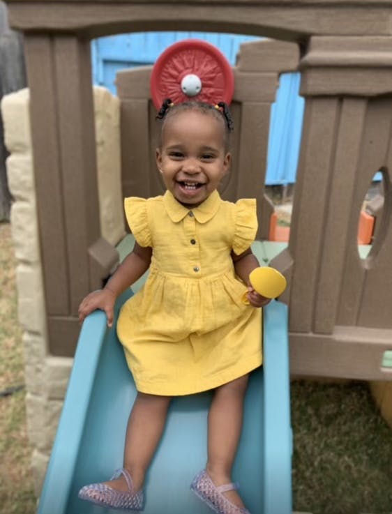 Child in a yellow dress sitting on a blue slide
