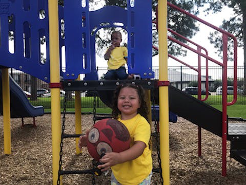 Two children on a playground structure, one holding a red ball