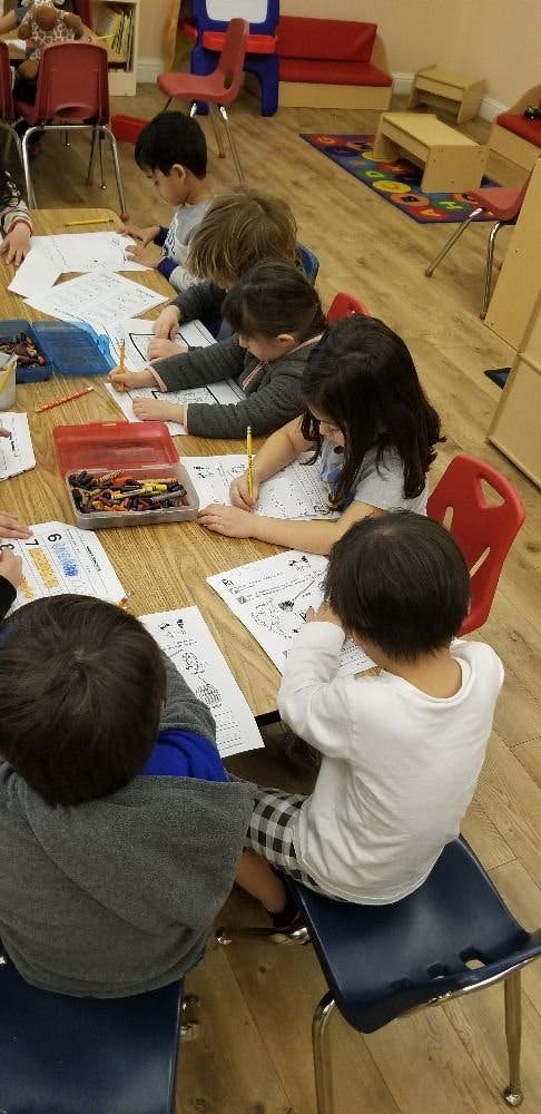 Children sitting at a table drawing on papers in a classroom