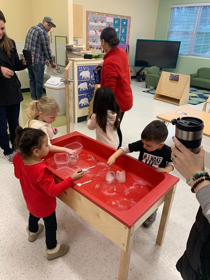 Children playing at a red sensory table with water and ice