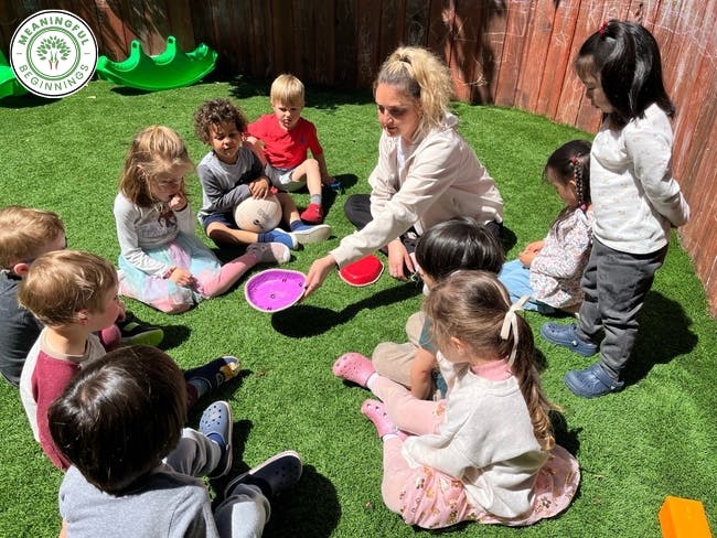 Adult and children sitting in a circle on artificial grass
