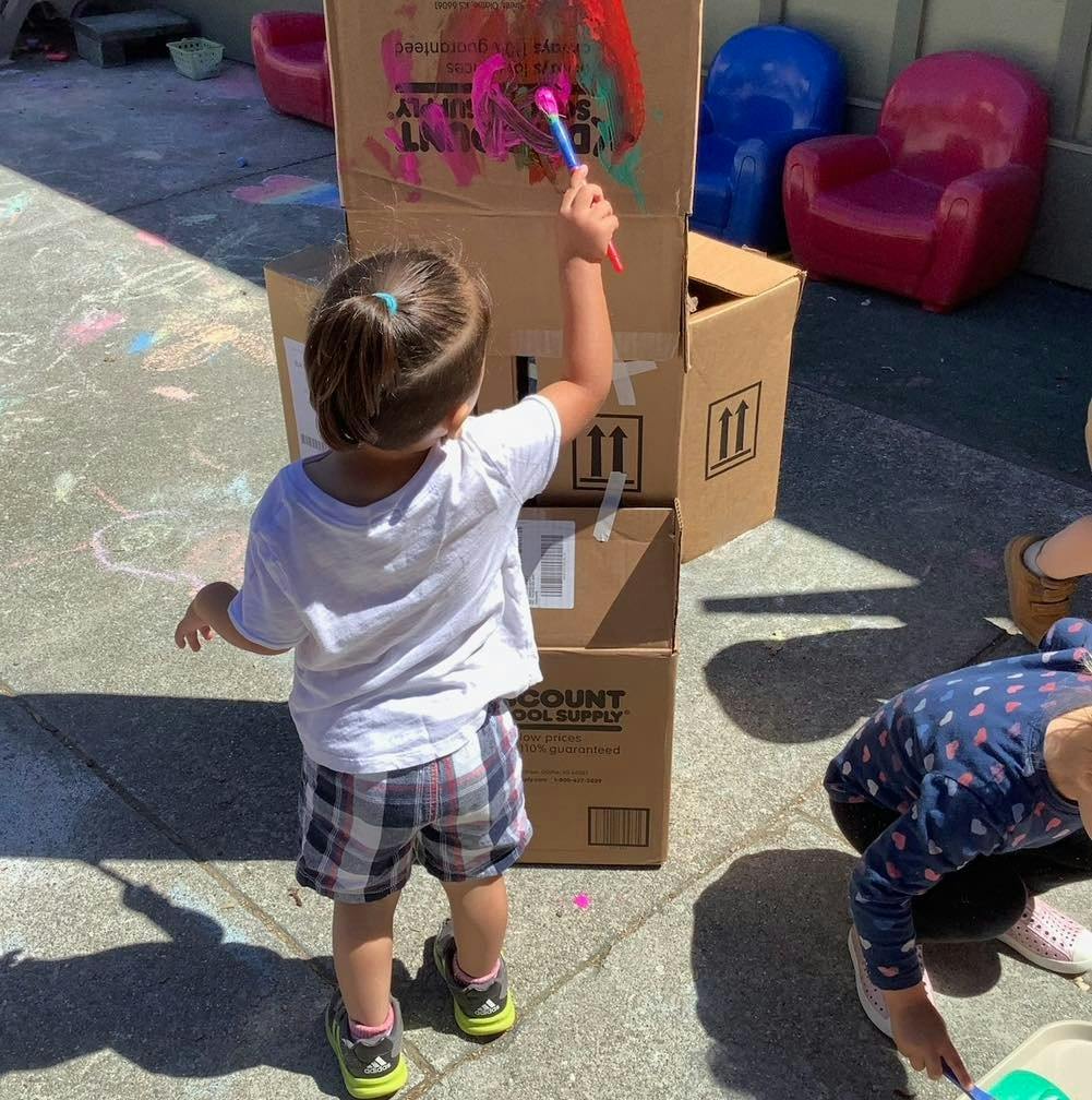 Child painting on a cardboard box outside