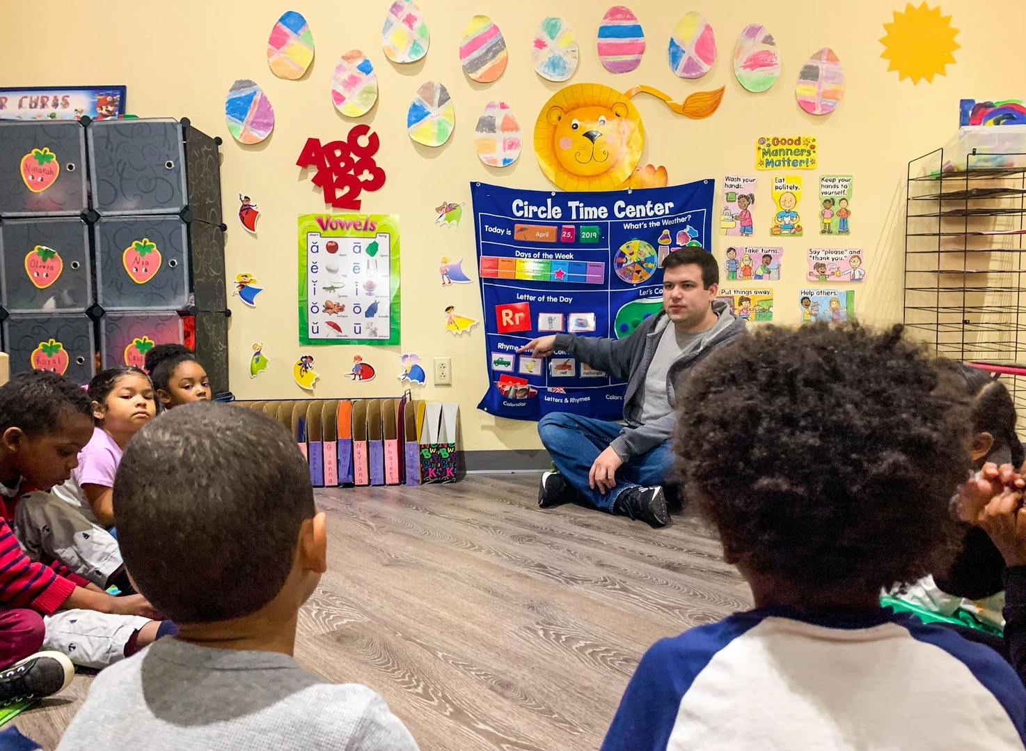 Adult pointing to a chart while sitting on the floor with children in a classroom