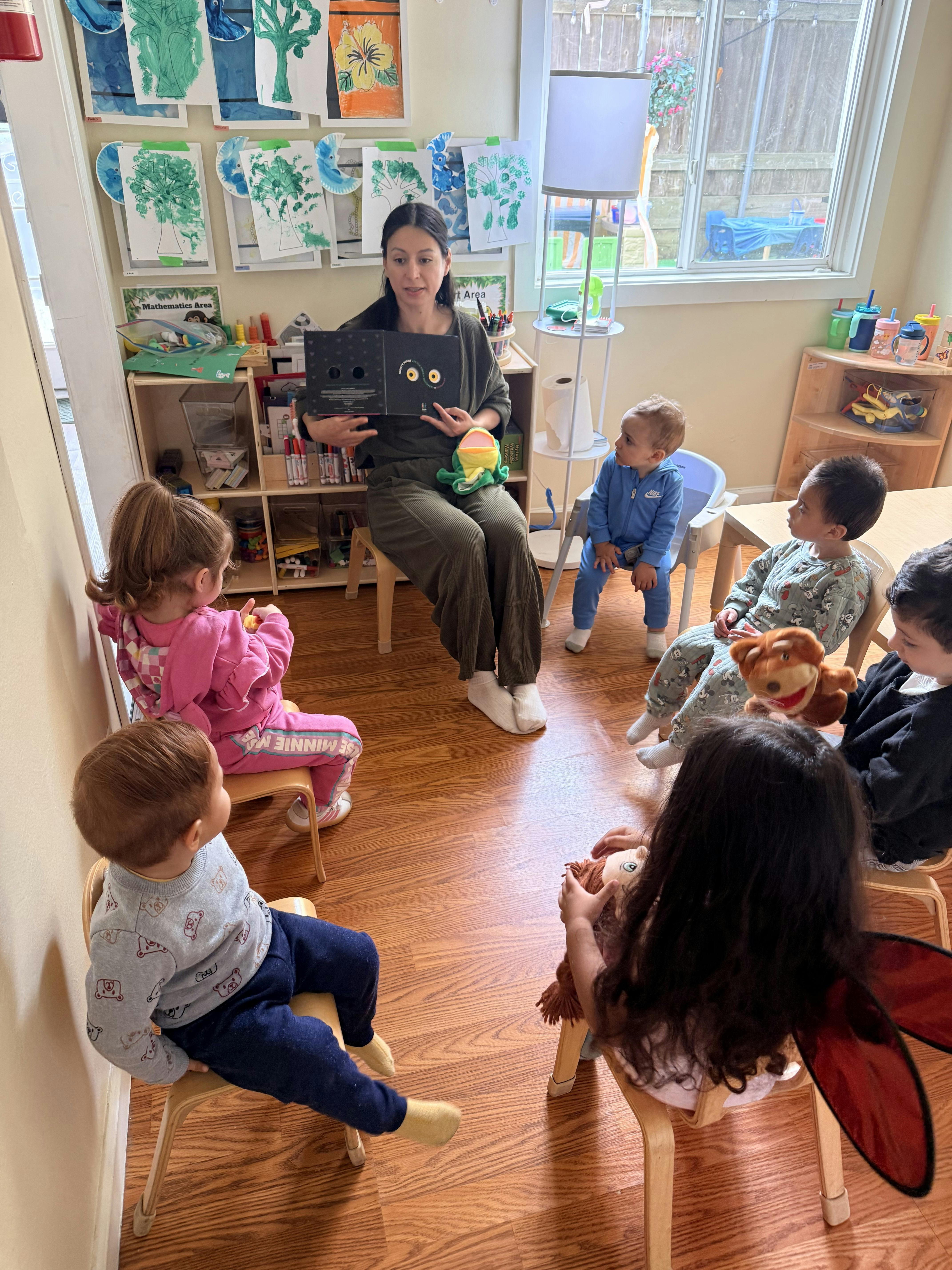 Adult person reading a book to a group of children in a classroom