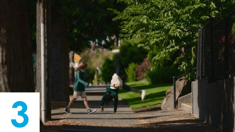 Child doing a cartwheel on a sidewalk next to another child walking