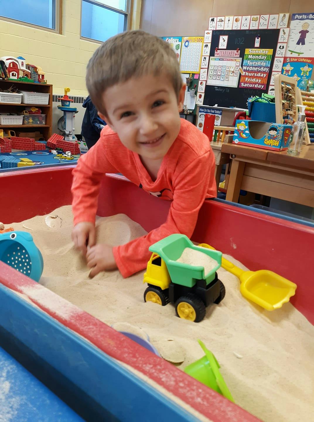 Child playing in a sand table with a toy truck and shovel