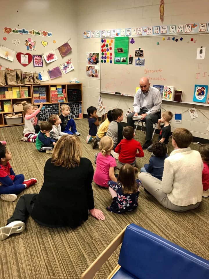 Adult reading to a group of children and adults in a classroom