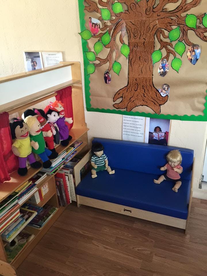 Puppets on a shelf next to a blue couch with two dolls in a classroom