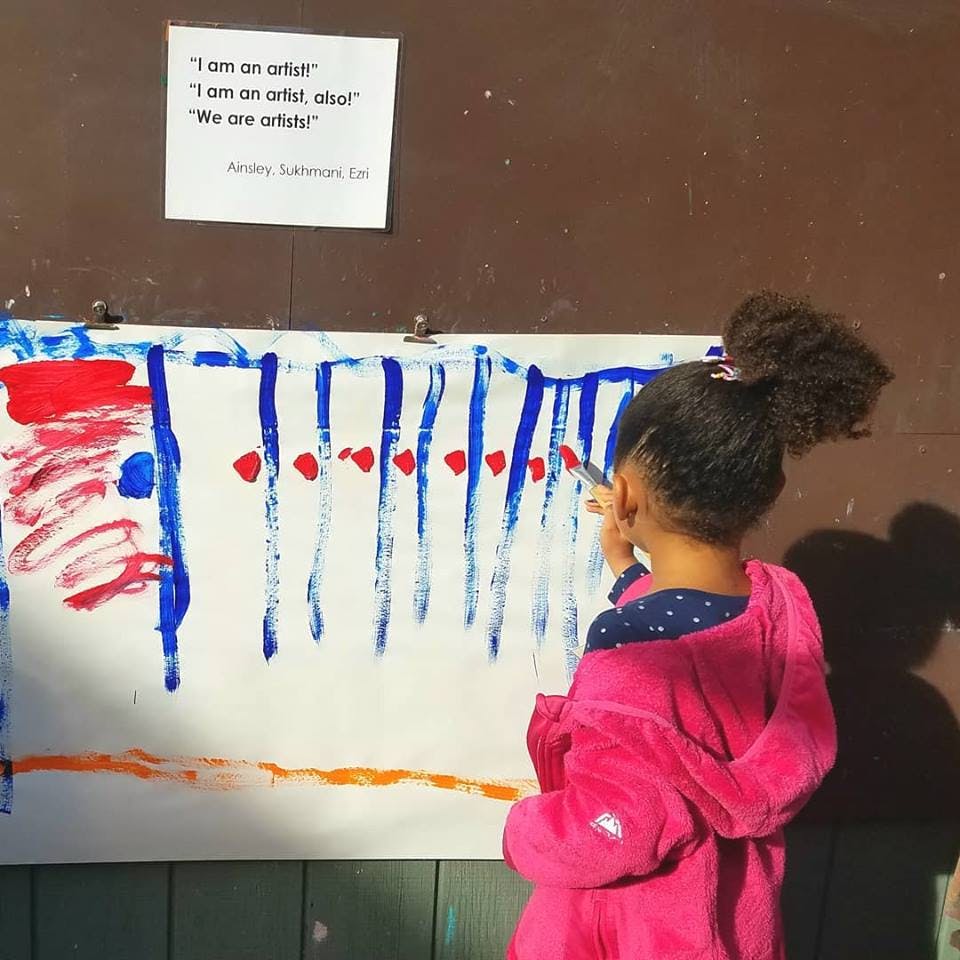 Child painting on a large white canvas with blue and red paint