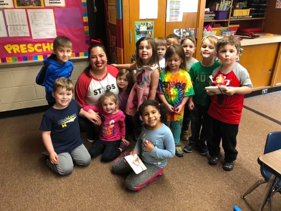 Adult and multiple children posing for a photo in a classroom