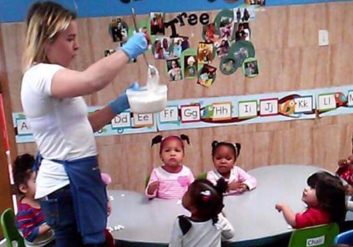 Person in blue gloves pouring liquid for children in a classroom