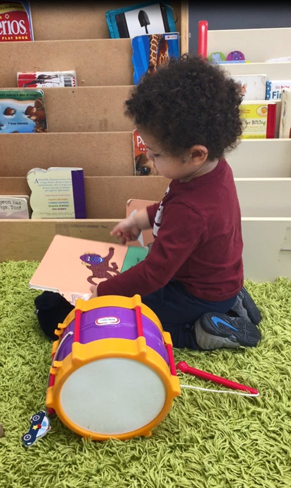 Child on floor looking at a book next to a toy drum
