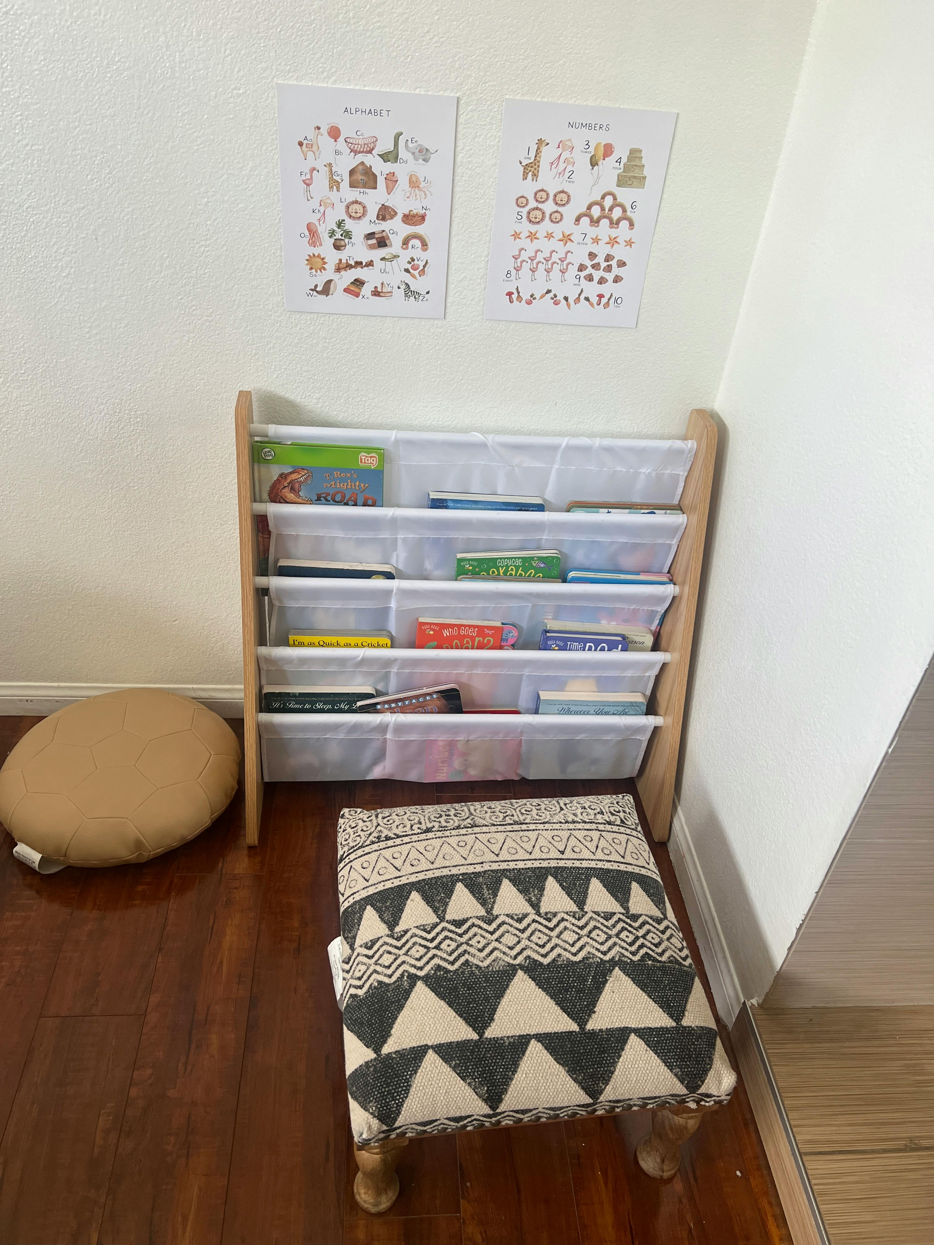 Bookshelf with books, a floor cushion, and a patterned stool