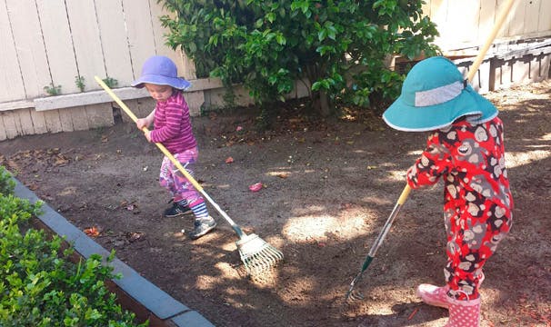 Two children raking dirt in a yard