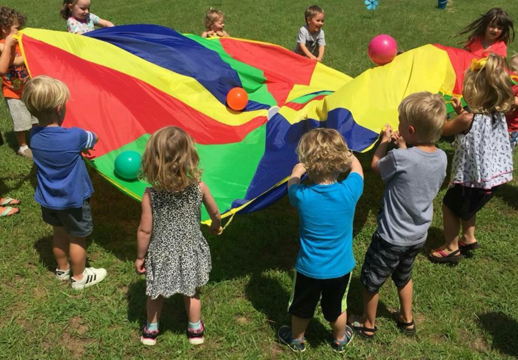 Children playing with a colorful parachute and balls outdoors