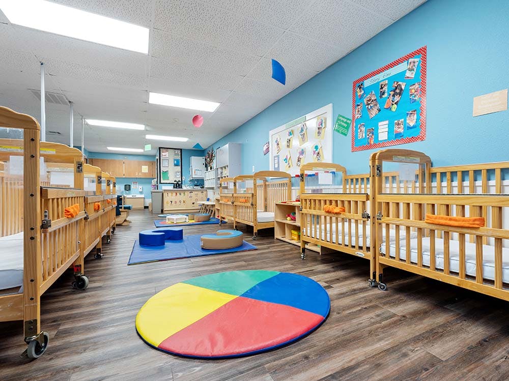A room with multiple wooden cribs, a colorful mat on the floor, and blue walls