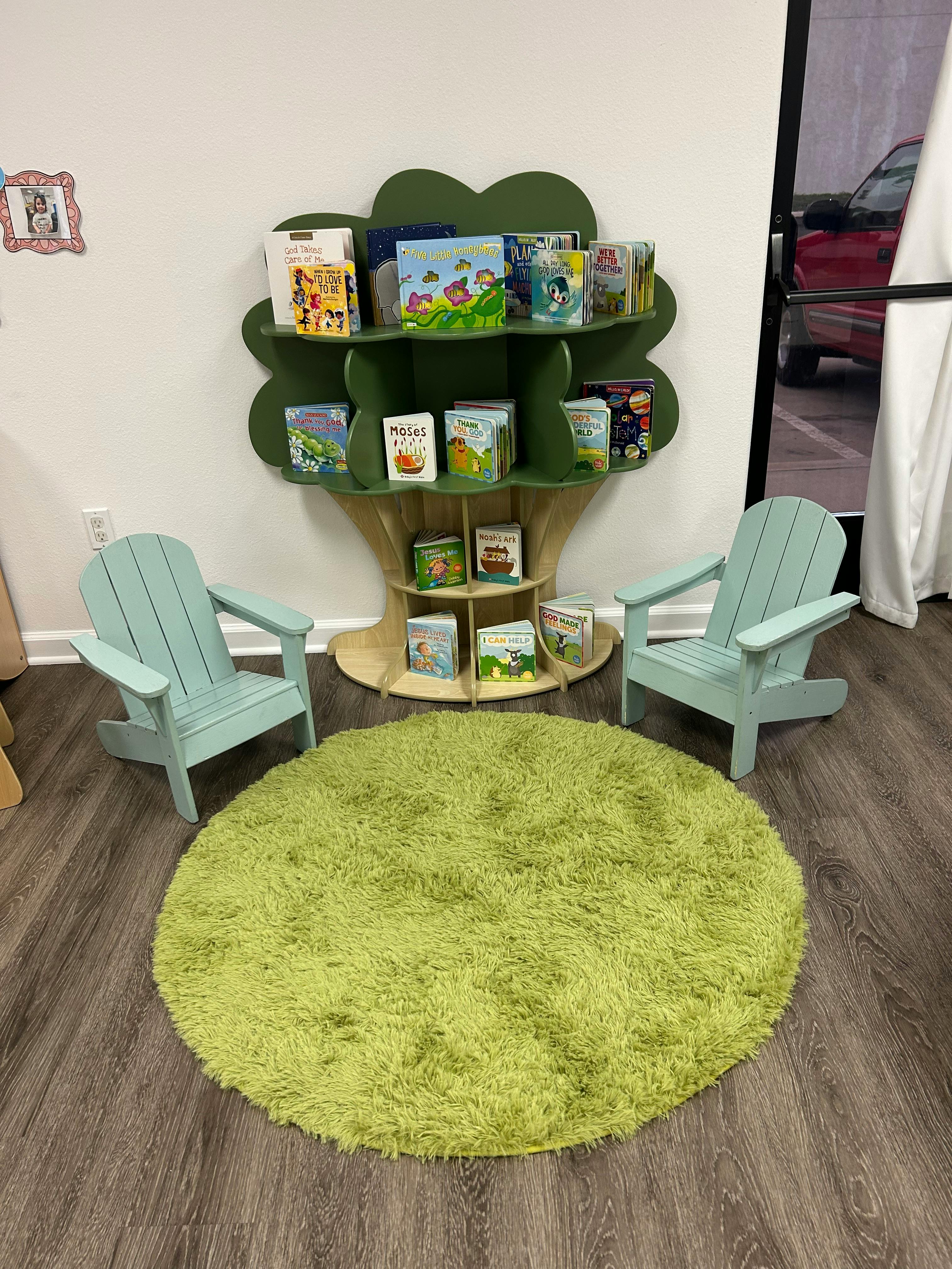 Tree-shaped bookshelf with books, two small chairs, and a round rug