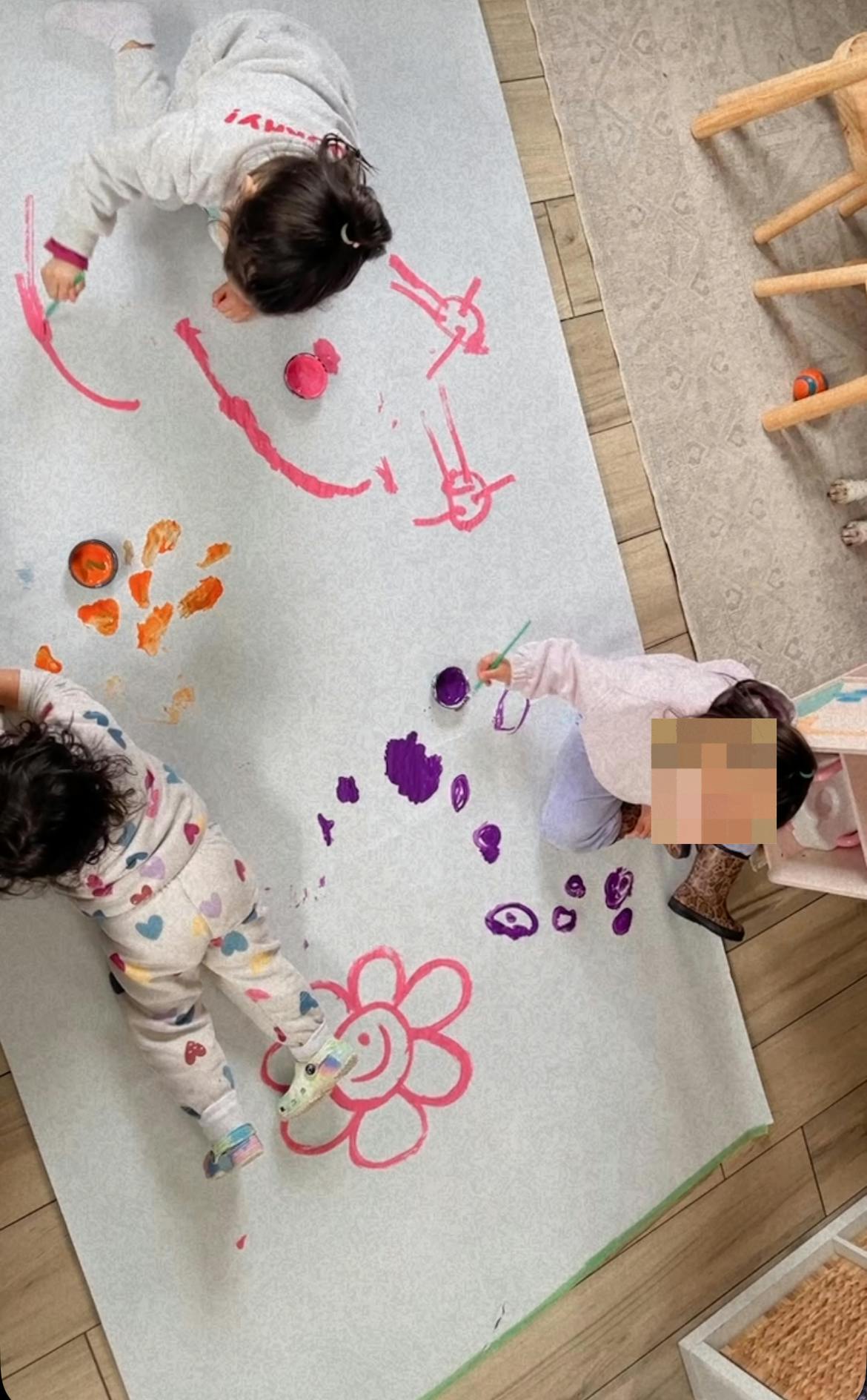 Three children painting on a large white sheet on the floor