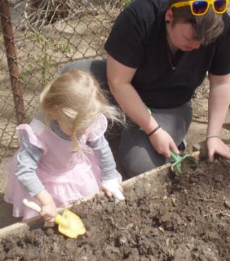 Adult and child digging in garden bed with small tools