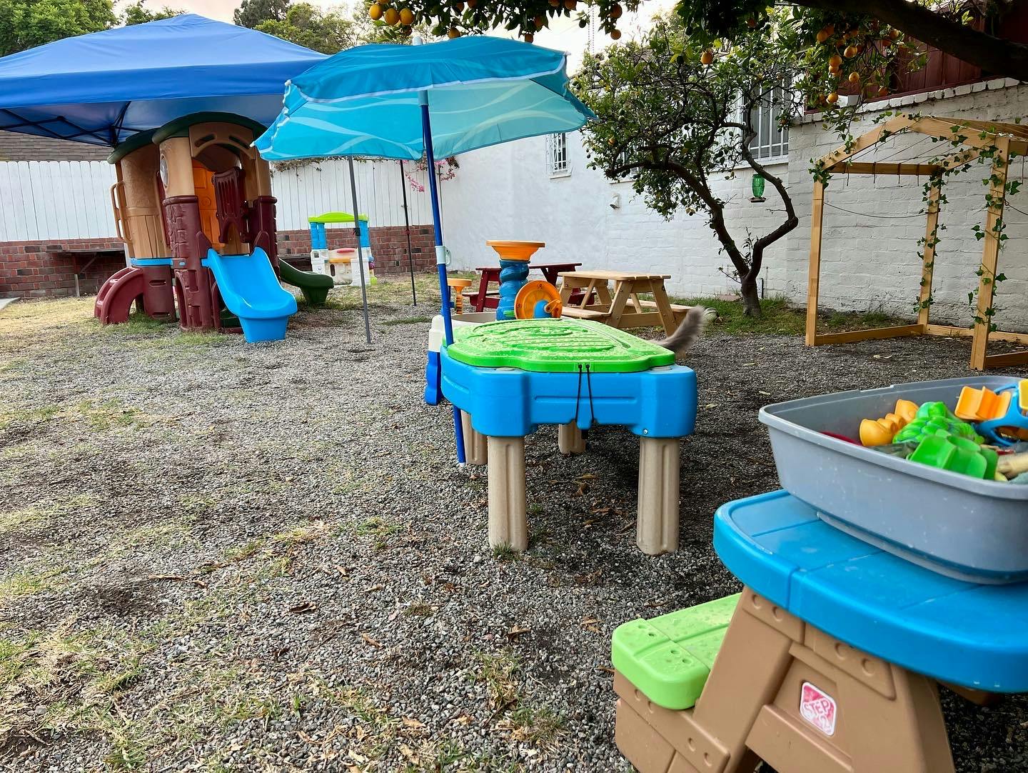 Outdoor play area with a playhouse, sand and water table, and toys