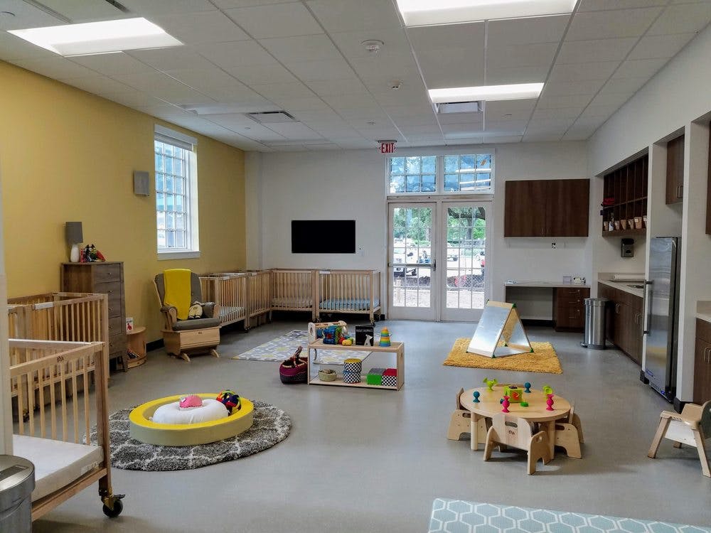 Daycare room with cribs, small tables, and play areas