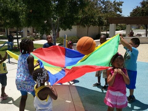 Children playing with a colorful parachute and a basketball