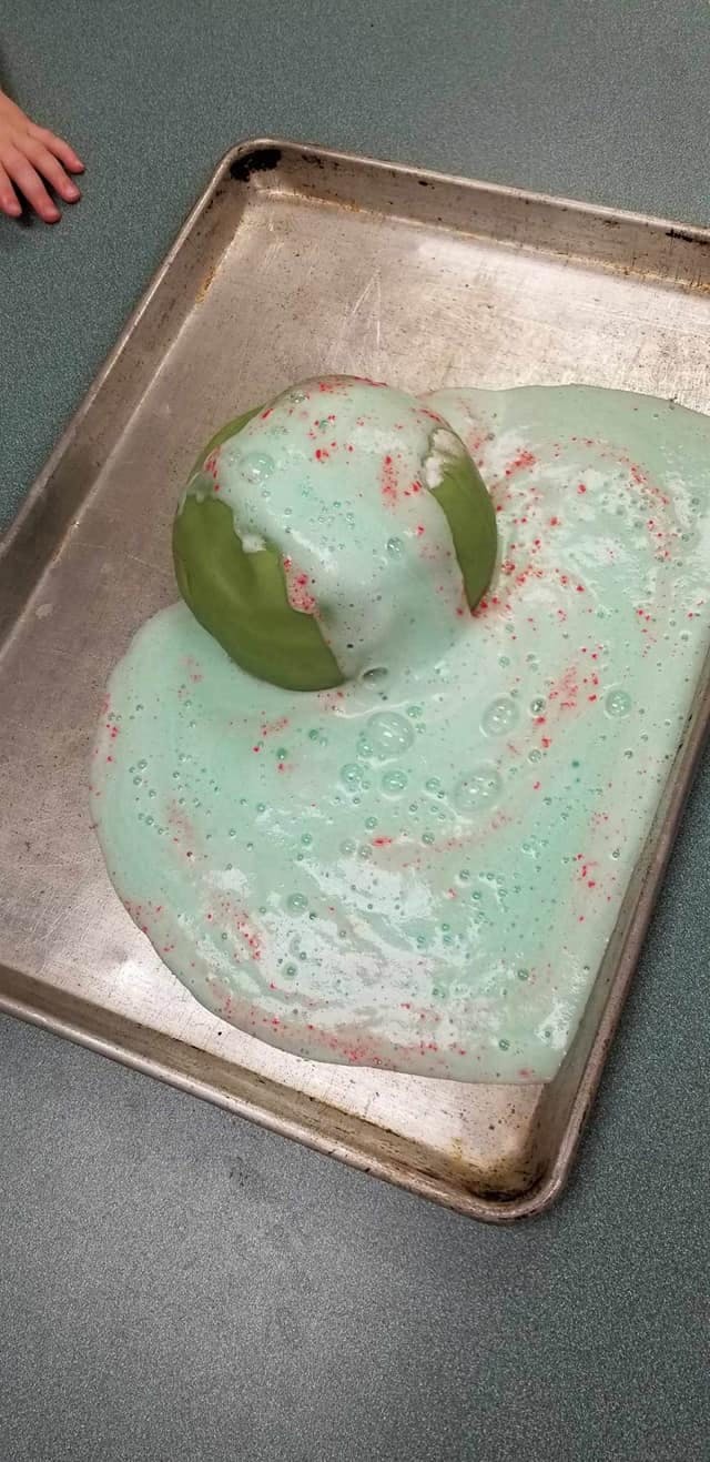 Green object with light blue foam and red sprinkles on a metal tray