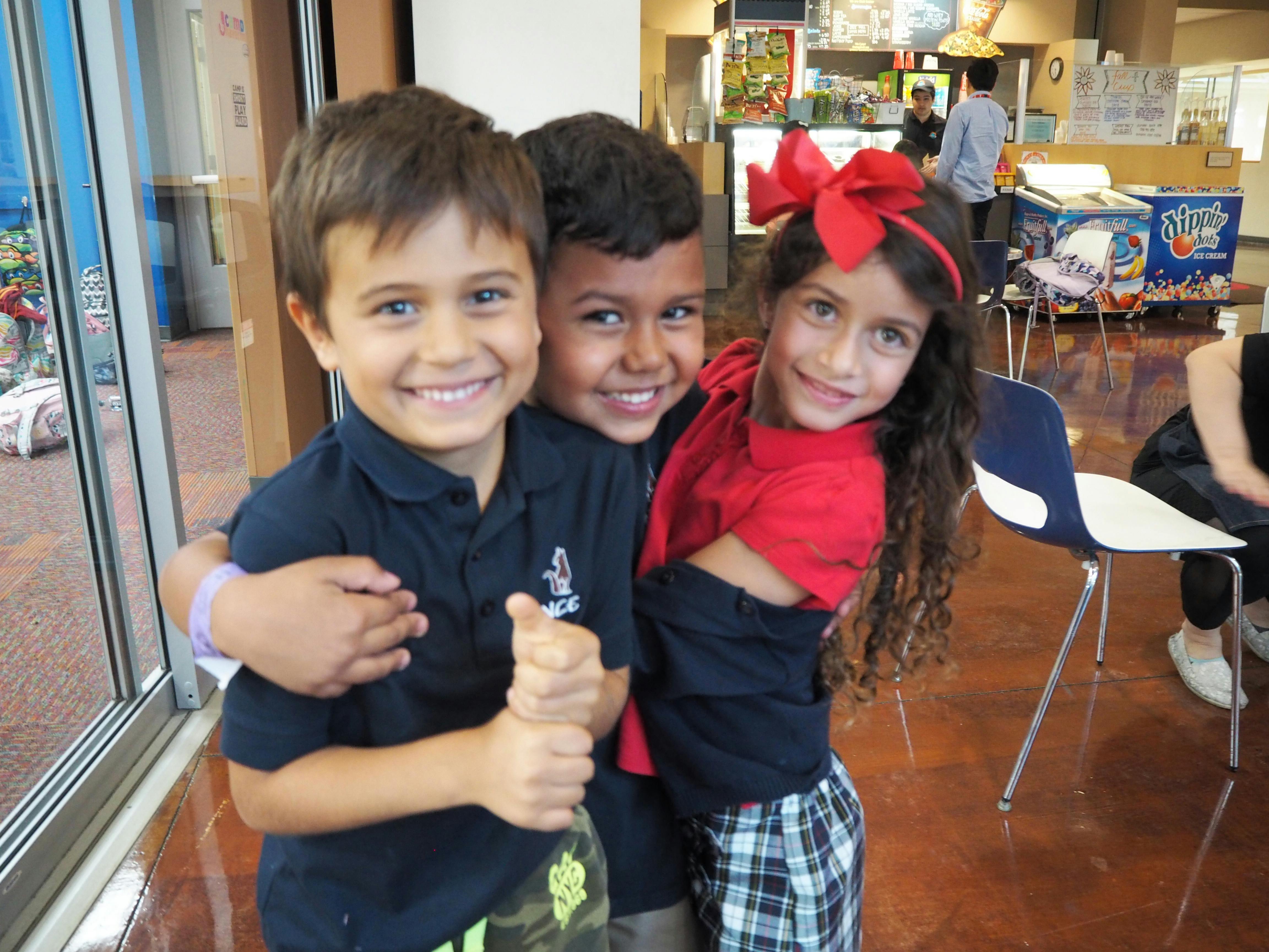 Three children smiling and posing together, one giving a thumbs up