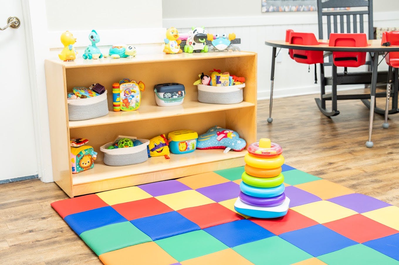 Colorful stacking rings on a play mat next to a toy shelf in a classroom