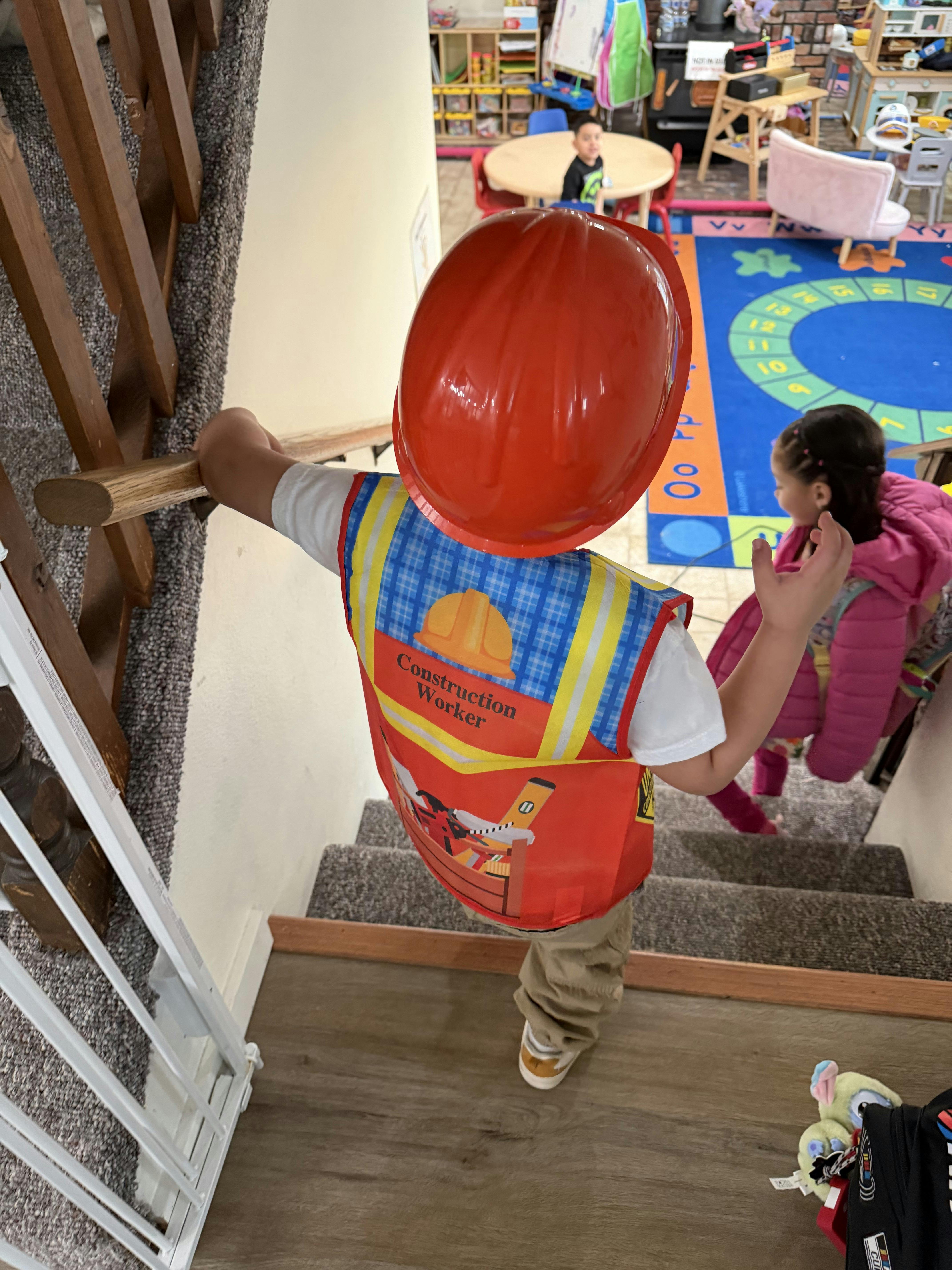 Child in a construction worker vest and helmet holding a stair rail