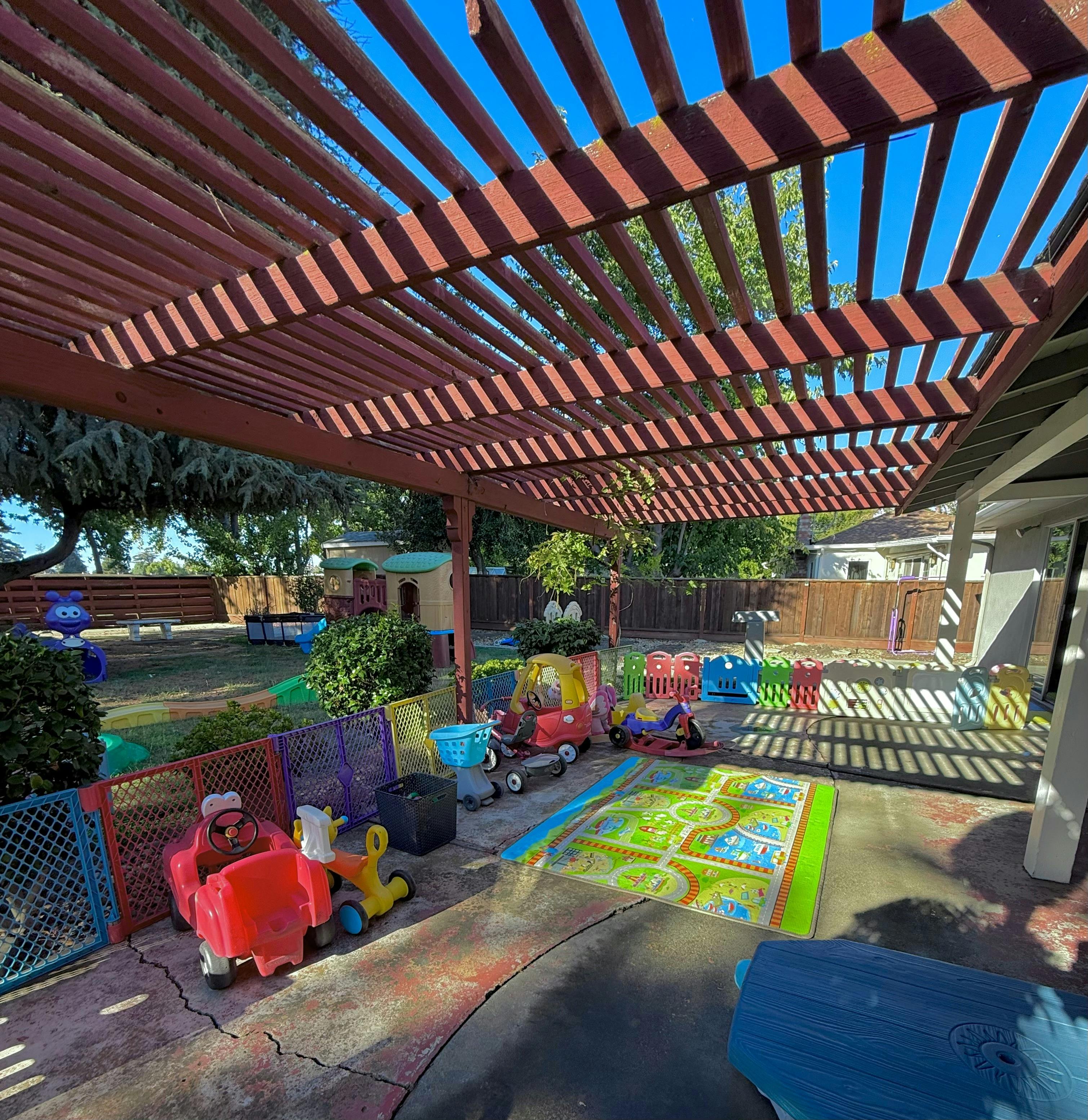Play area for children with ride-on toys and a play mat under a wooden pergola
