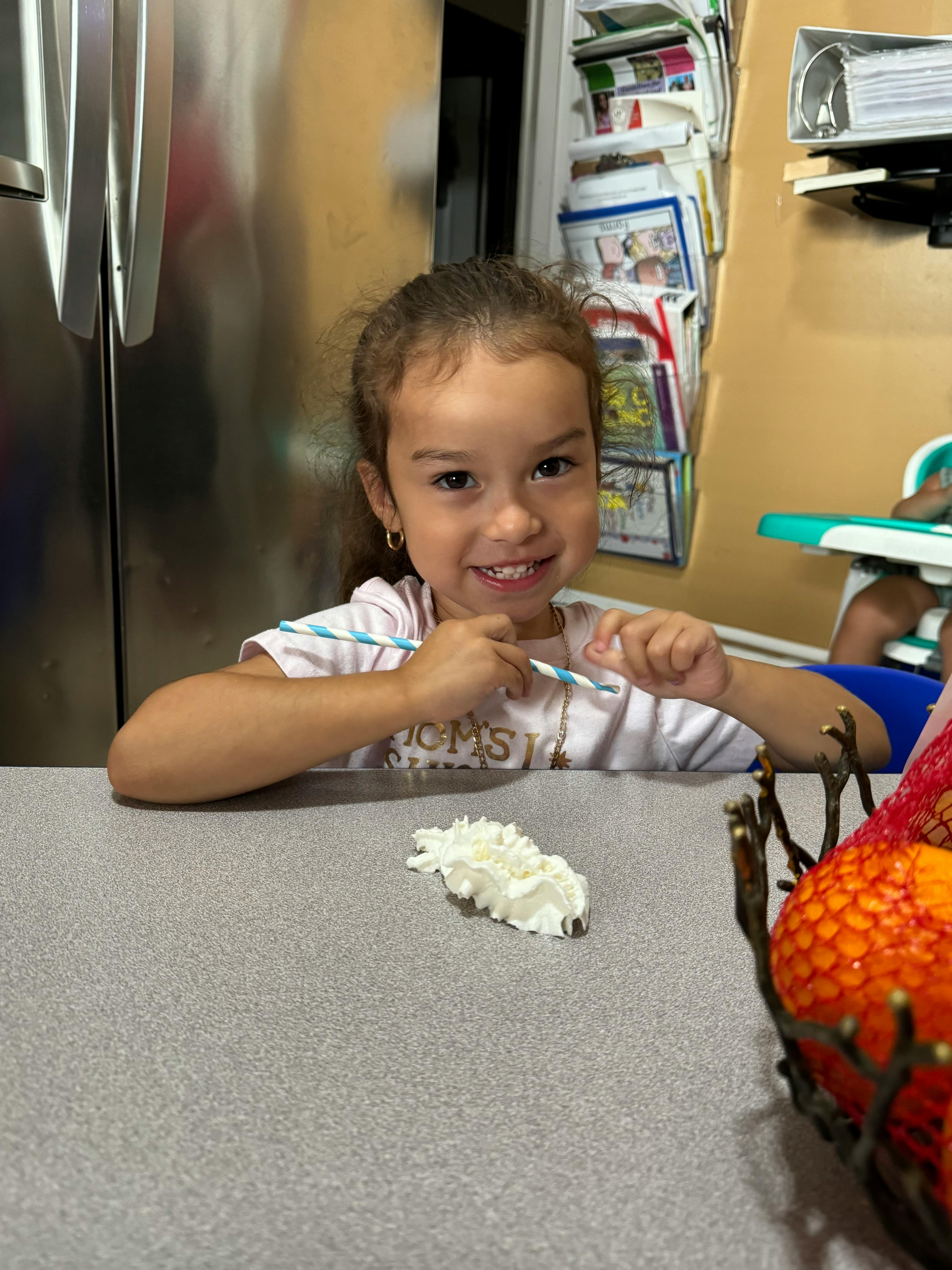 Child sitting at a table with a straw and whipped cream