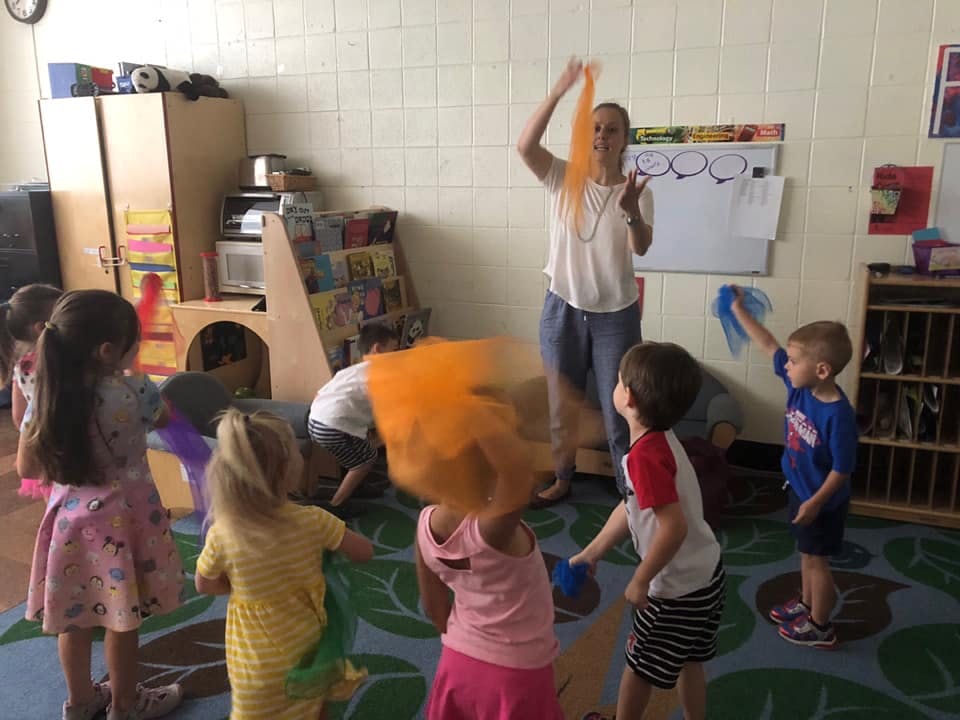 Adult and children playing with colorful scarves in a classroom
