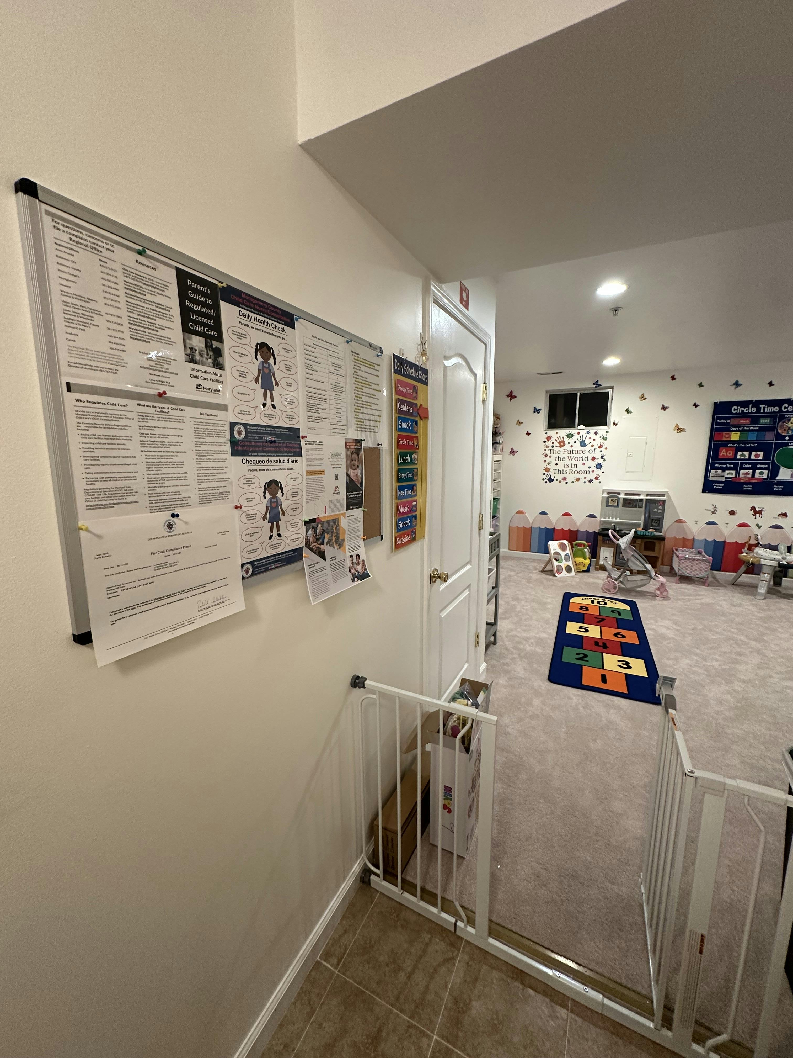 Bulletin board with papers and a child safety gate leading to a room with carpeted room