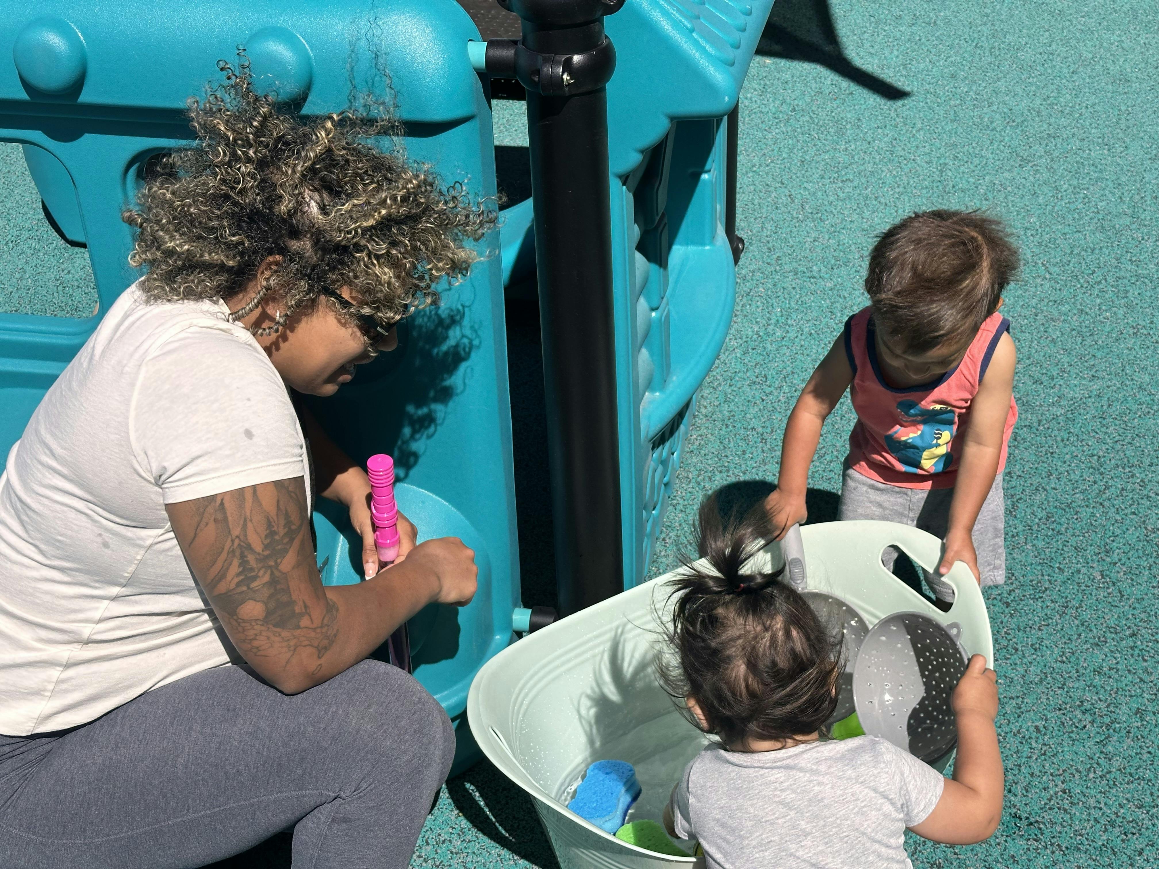 Adult and two children playing with water and toys at a playground