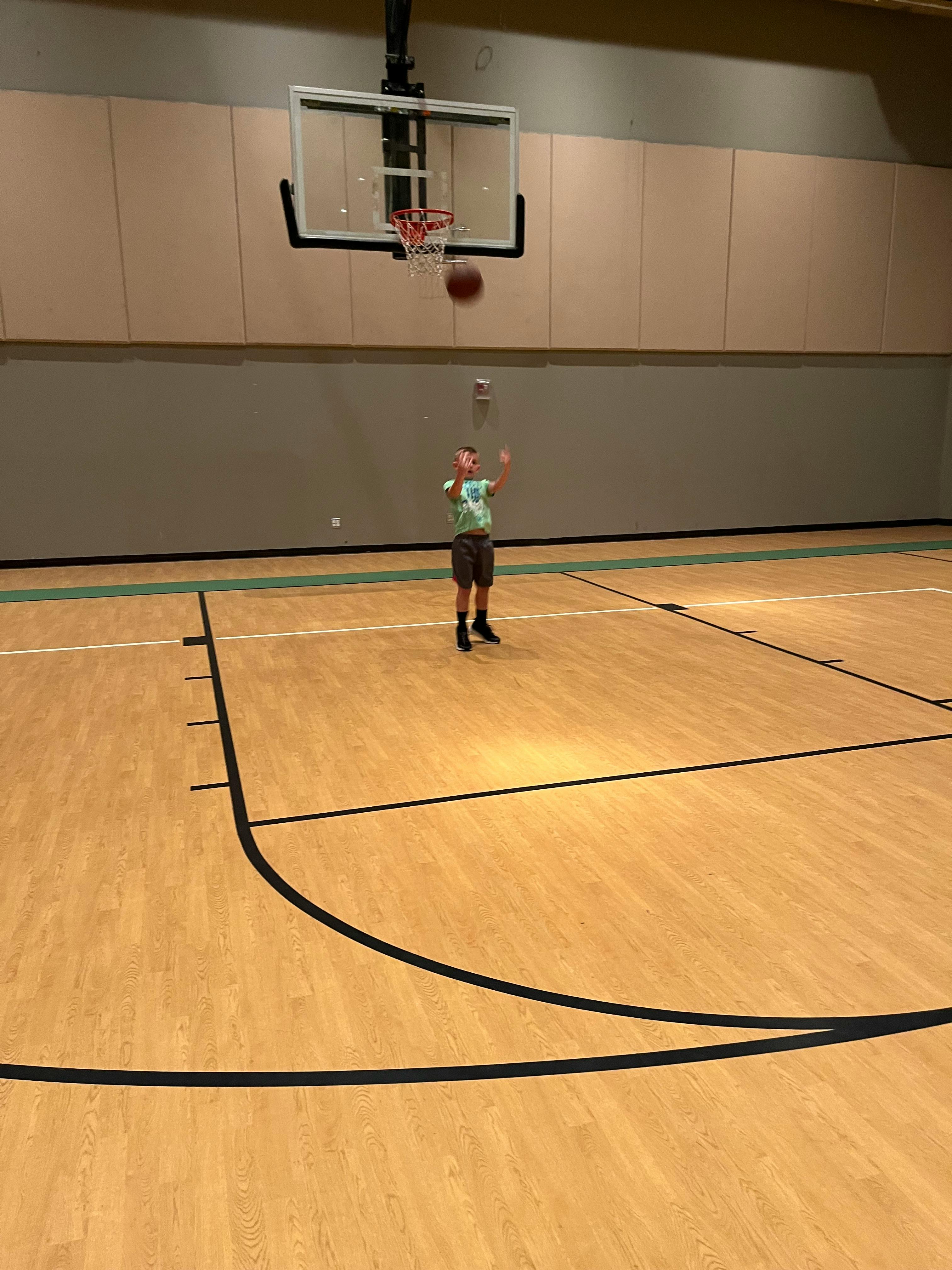 Child on a basketball court with a basketball near the hoop