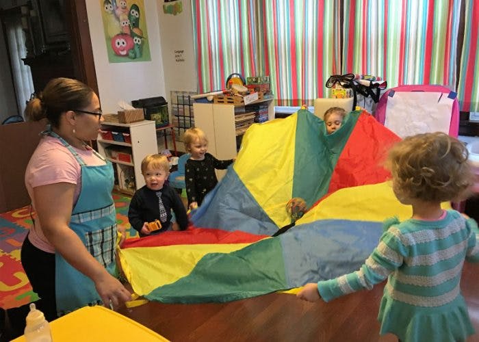 Adult and children playing with a colorful parachute in a classroom