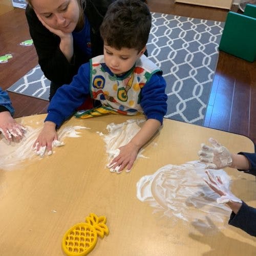 Person and child playing with white foam on a table