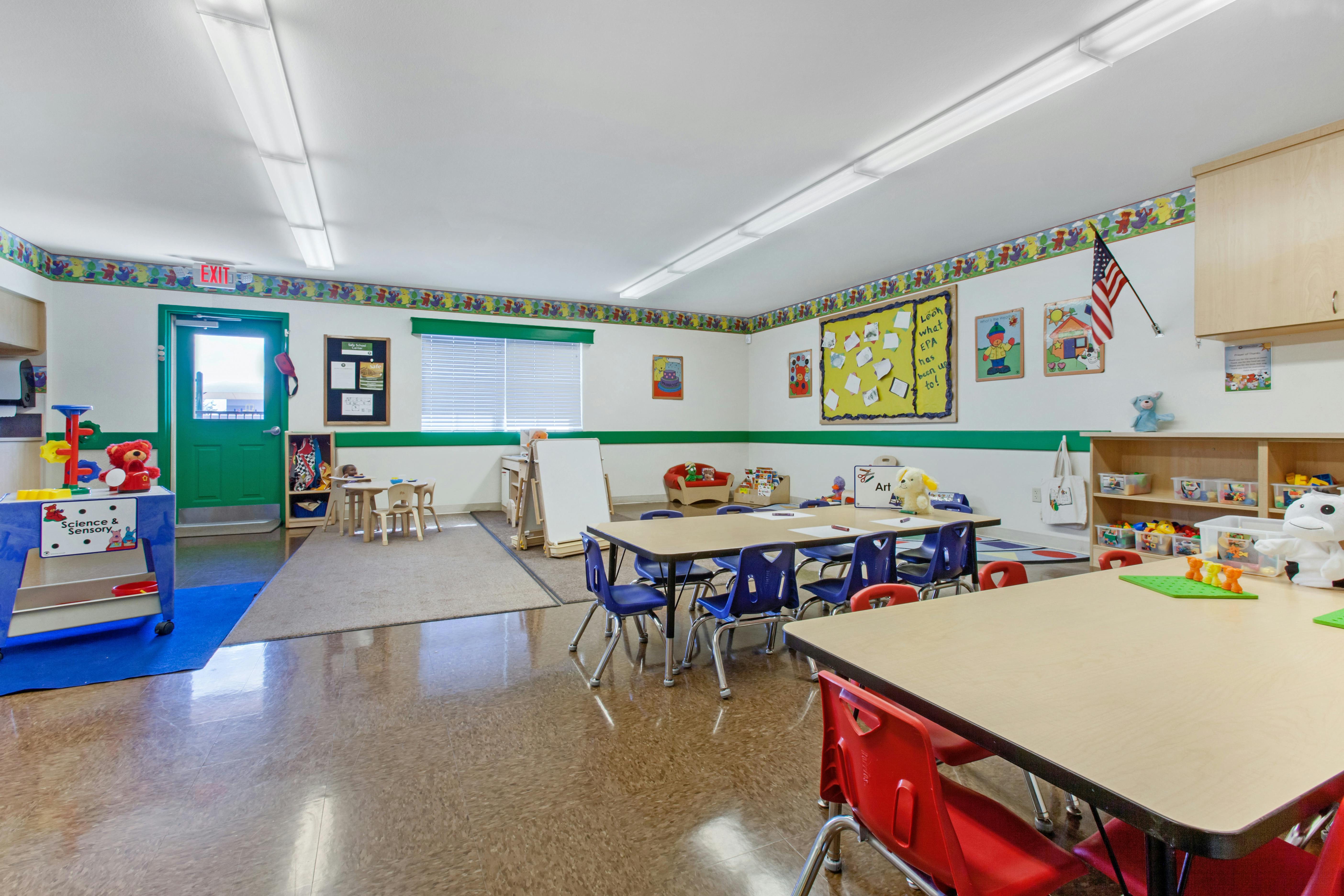 Classroom with child-sized tables and chairs, a science and sensory cart, and wall decorations