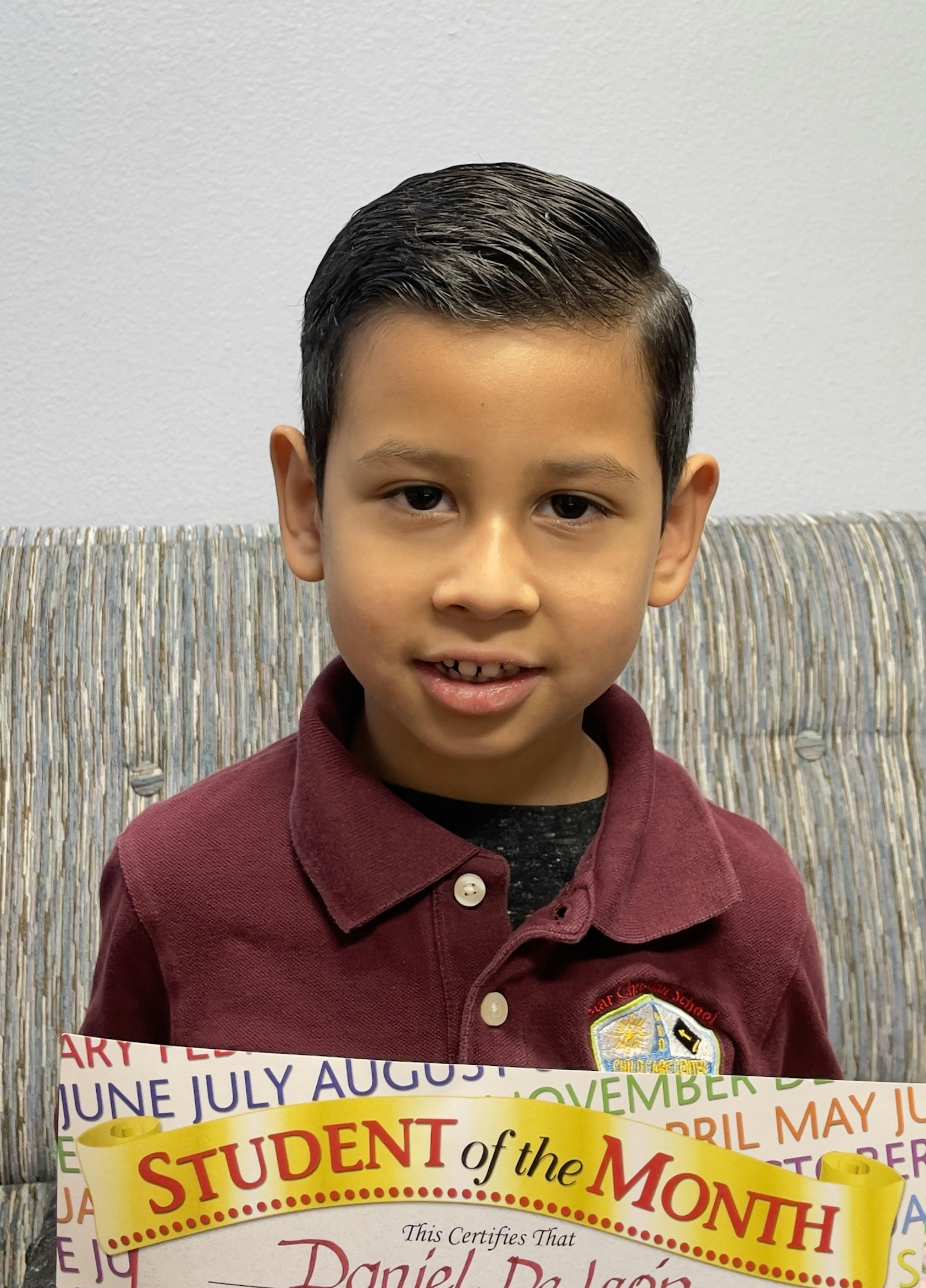 Child in a maroon polo holding a "Student of the Month" certificate