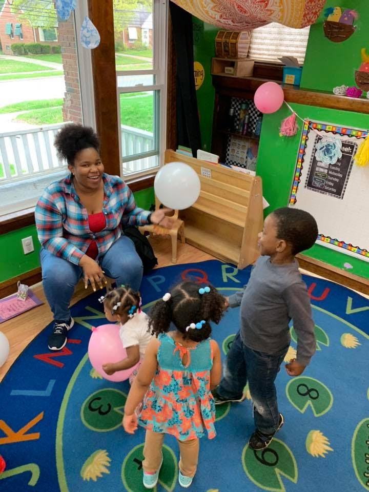 Person sitting on floor with three children playing with balloons